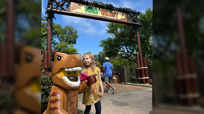 The writer’s daughter under the Dino Valley welcome sign with a Lego T-Rex